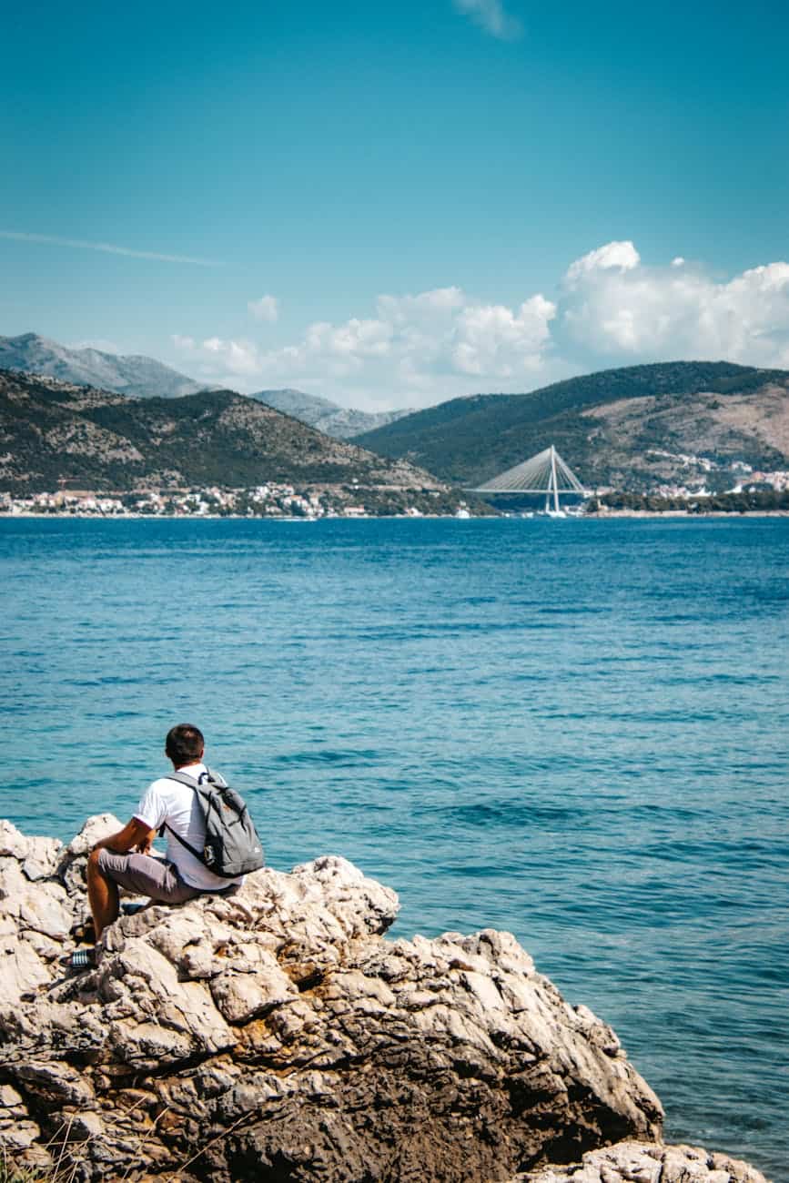 Young man enjoying the coastal views of the Adriatic Sea and the modern bridge in Dubrovnik during a Mediterranean cruise port day.