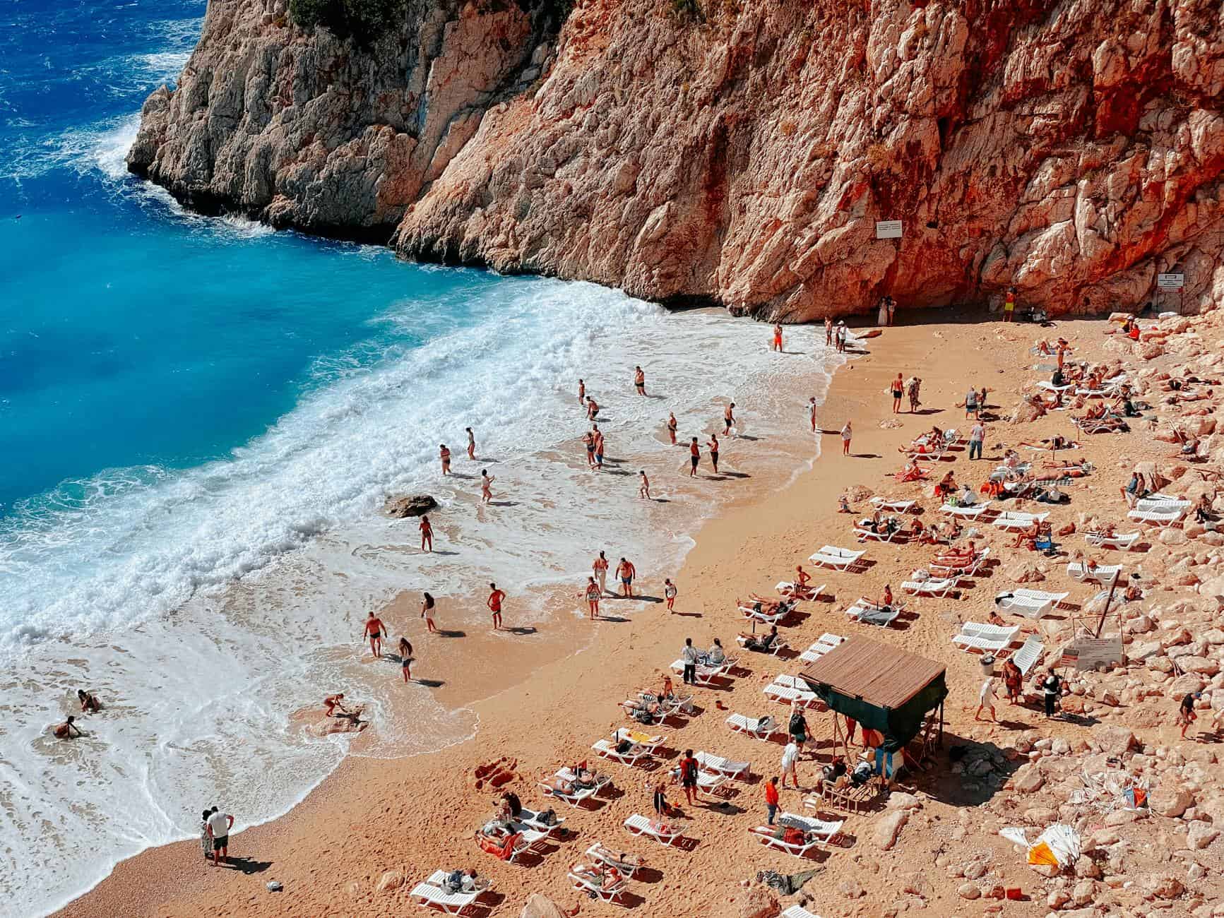 Aerial view of a vibrant, busy Mediterranean beach with turquoise water and umbrellas, a top leisure activity for cruise guests.